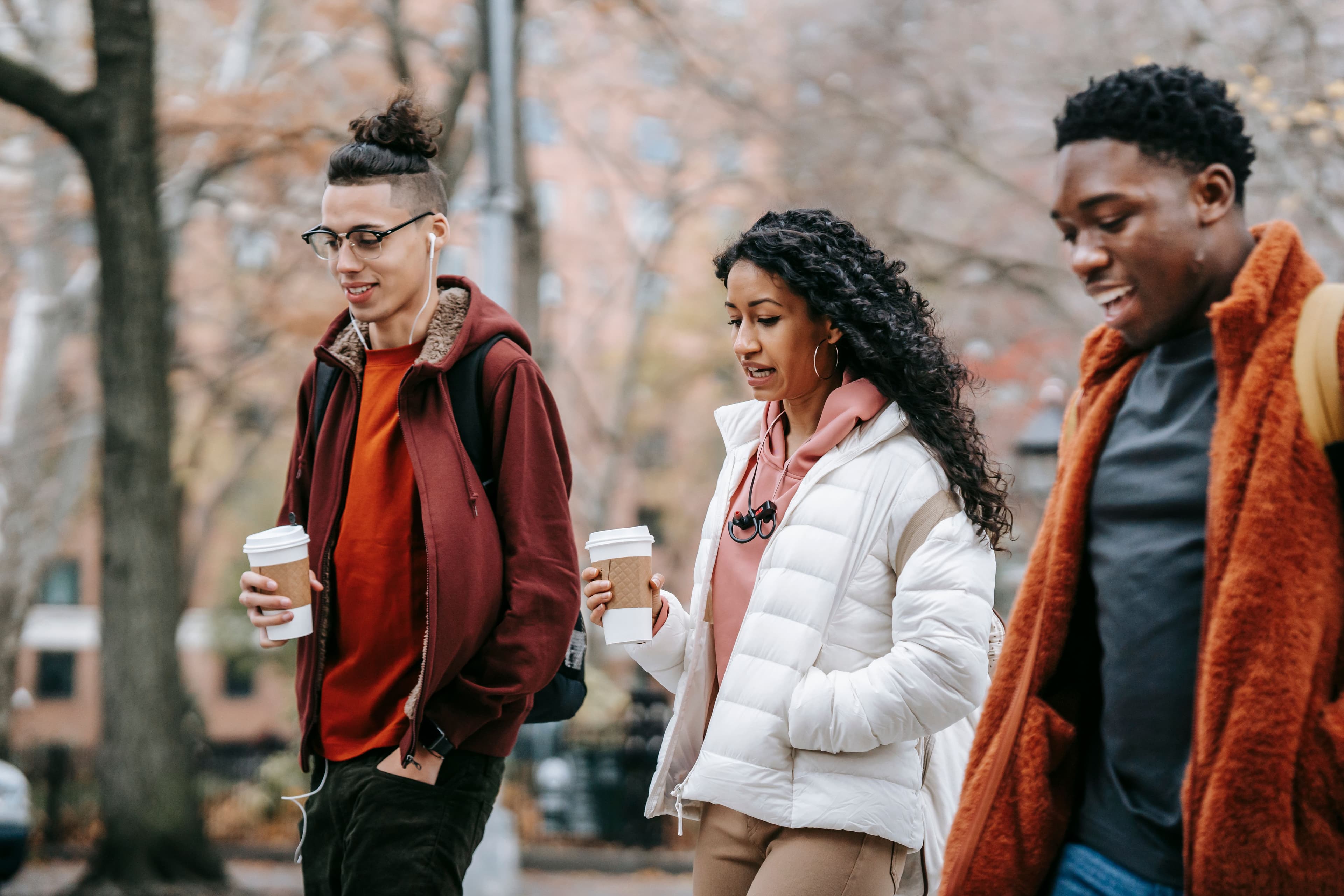 Three people walking together outdoors with coffee cups.